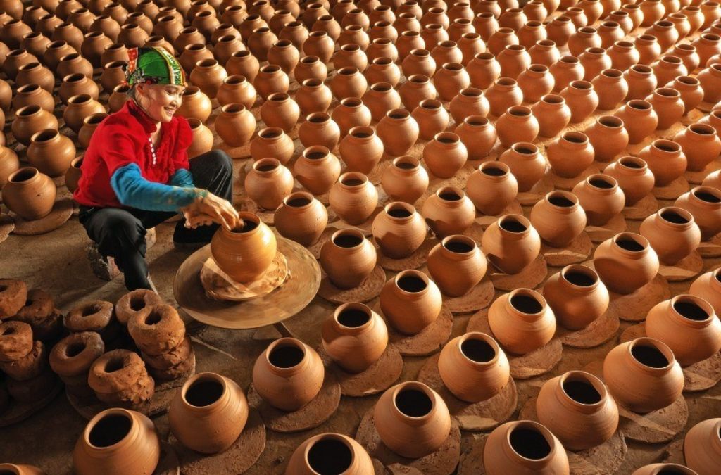 Người thợ tạo hình bình gốm trên bàn xoay giữa những hàng sản phẩm gốm tại Phù Lãng