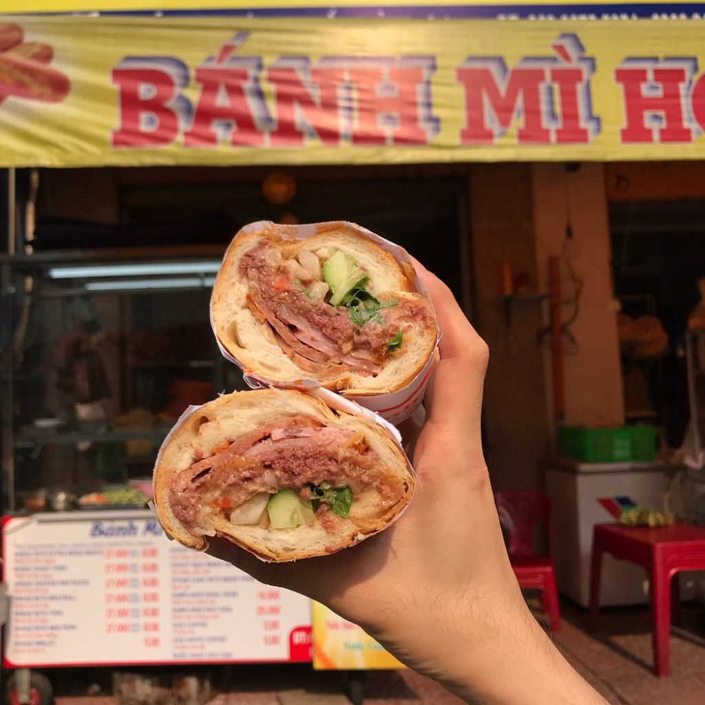 Hai nửa bánh mì Hồng Hoa kẹp thịt và dưa leo trước cửa tiệm