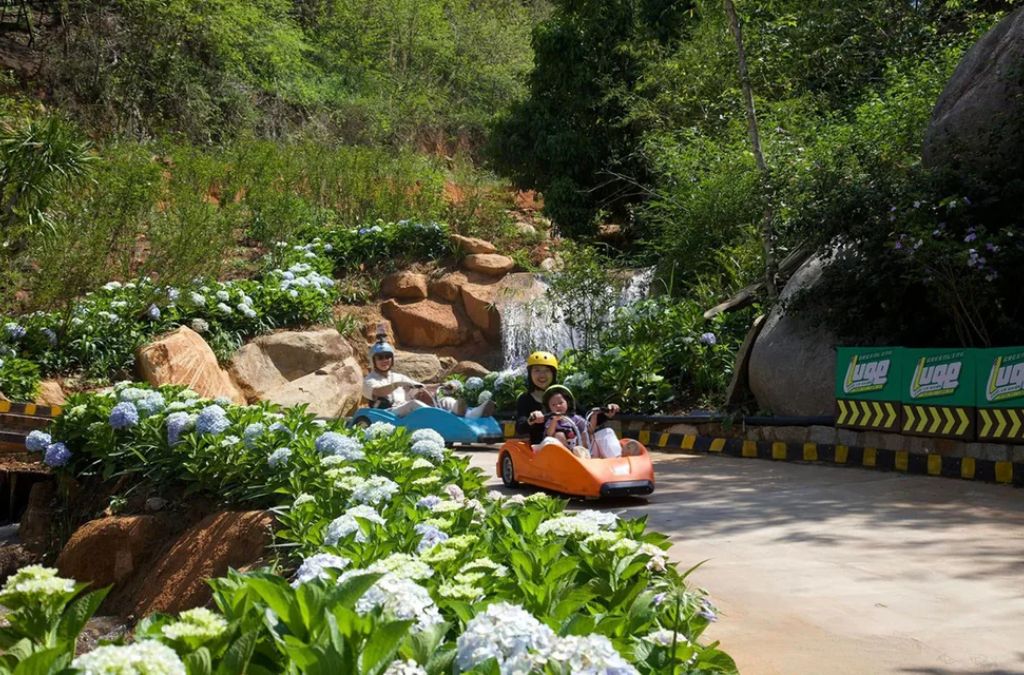 Người chơi xe trượt Greenline Luge trên đường đua giữa vườn hoa