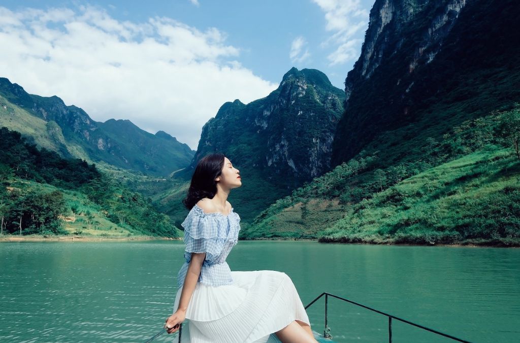 Người ngồi trên thuyền giữa sông Nho Quế và những dãy núi đá