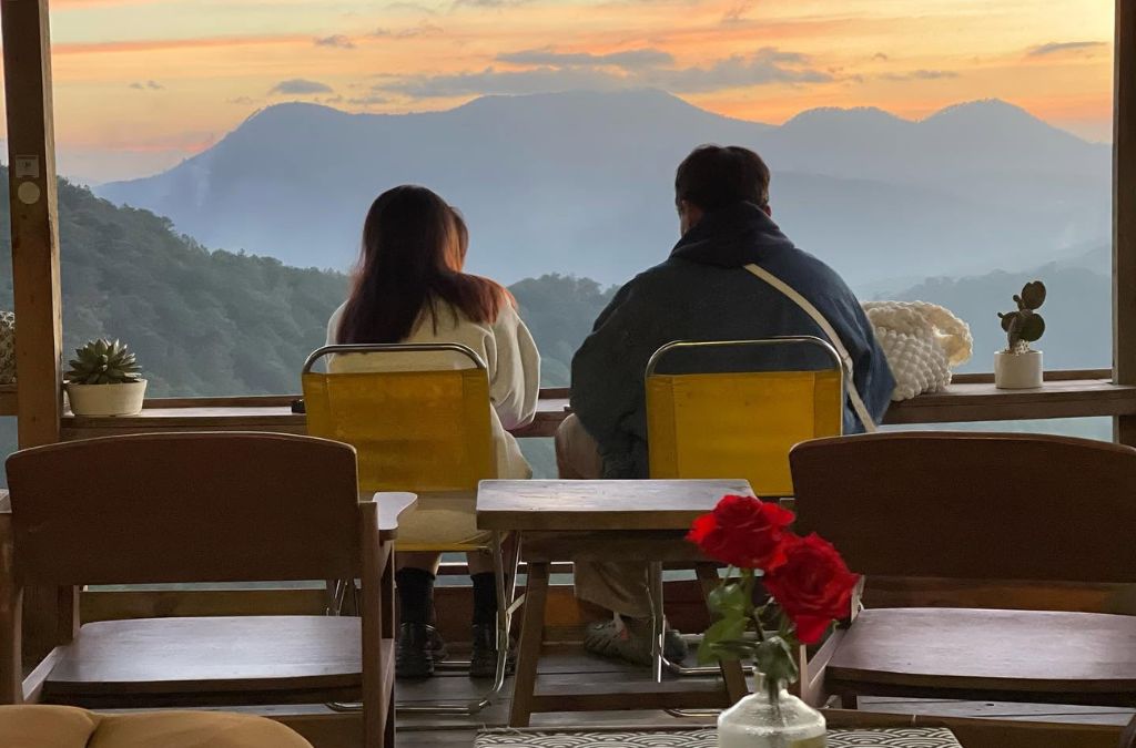 Hai người ngồi bên cửa sổ ngắm núi đồi tại Rừng Na Uy Cafe