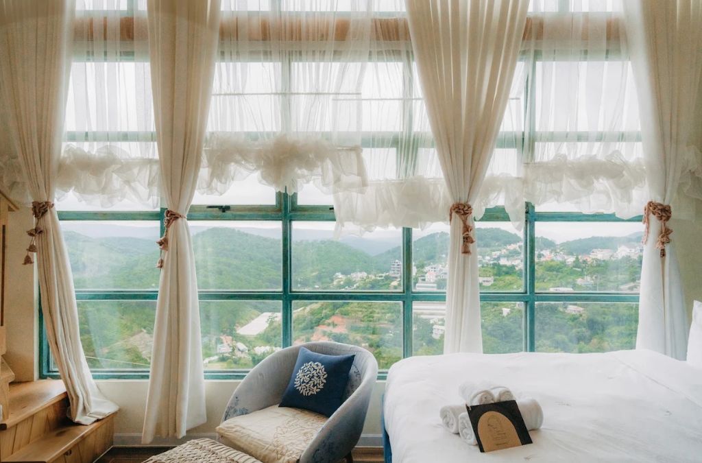 Phòng ngủ homestay Đà Lạt với cửa sổ lớn nhìn ra đồi xanh