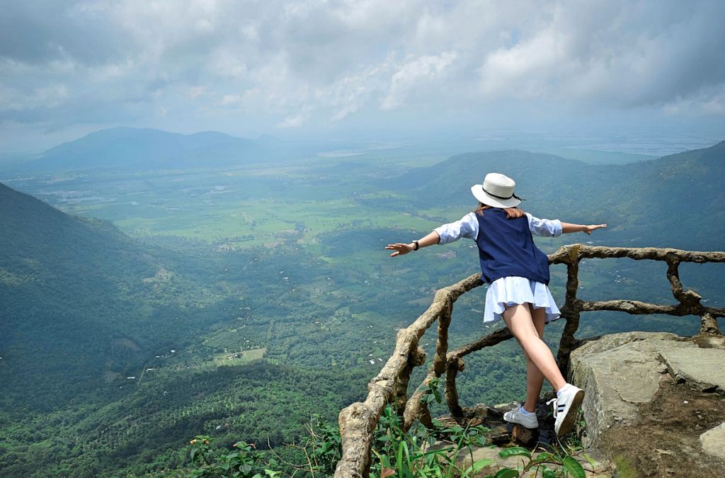 Một người đứng bên lan can tại điểm cao trên núi Cấm, nhìn xuống đồng bằng và núi rừng