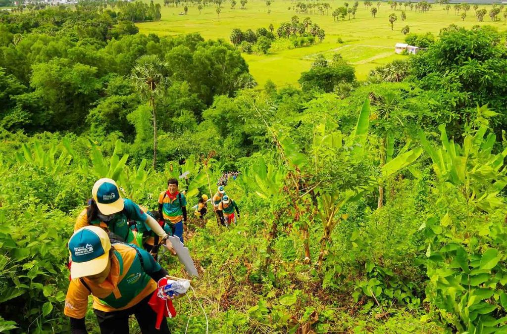 Nhóm người trekking theo lối mòn giữa cây cỏ xanh trên sườn núi Cấm