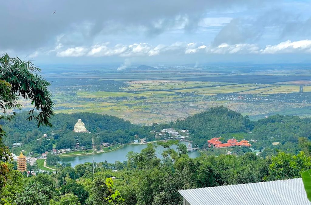 Đồng bằng An Giang nhìn từ đỉnh núi Cấm dưới trời nhiều mây, phía trước là hồ Thủy Liêm và rừng cây xanh