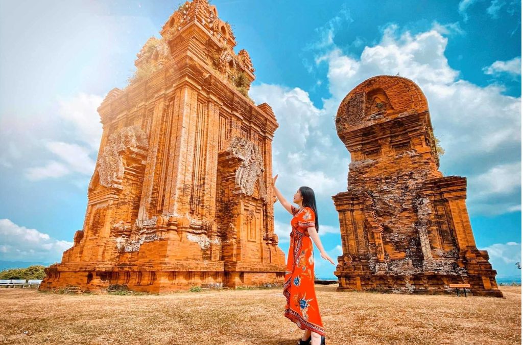 Một phụ nữ mặc áo dài đứng bên quần thể tháp Chăm Bánh Ít